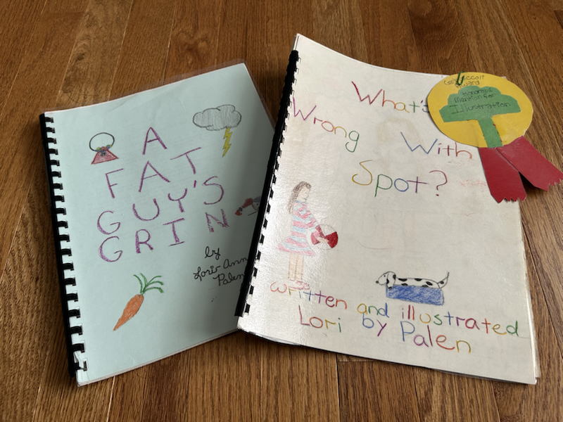 two bound booklets of Lori's school writing, one called A Fat Guy's Grin and the other called What's Wrong with Spot